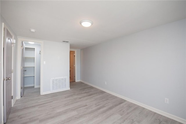 unfurnished bedroom with a walk in closet, a closet, and light wood-type flooring