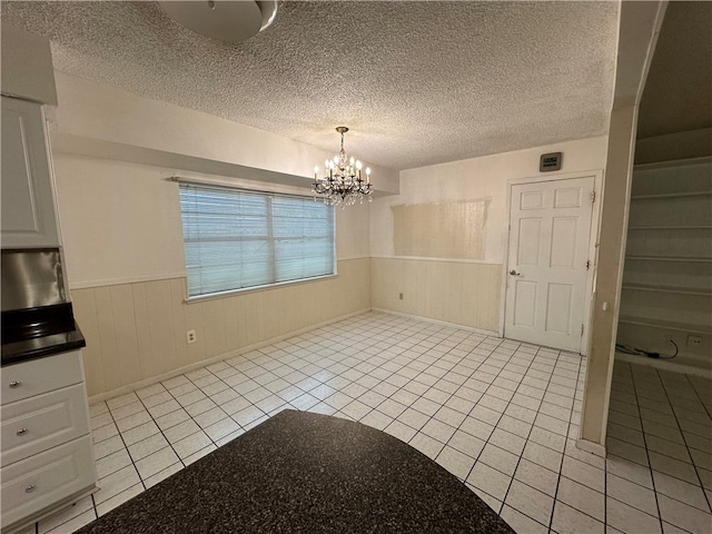 unfurnished dining area with a textured ceiling, light tile patterned floors, and a notable chandelier