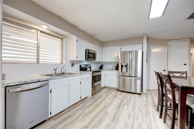 kitchen with appliances with stainless steel finishes, light stone counters, sink, light hardwood / wood-style floors, and white cabinetry