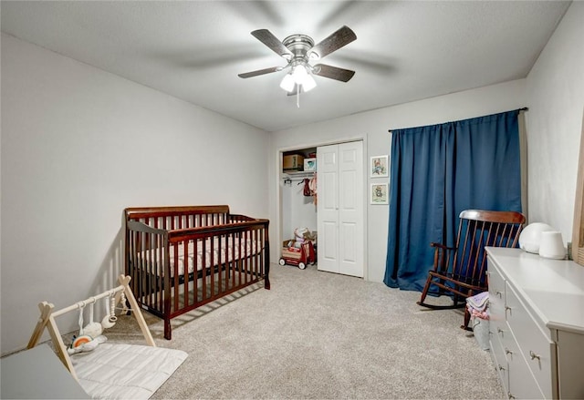 carpeted bedroom with ceiling fan, a closet, and a nursery area