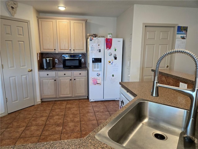 kitchen featuring light brown cabinets, tasteful backsplash, dark tile patterned flooring, white refrigerator with ice dispenser, and sink