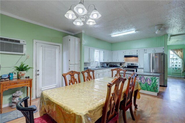 dining area featuring a textured ceiling, sink, an inviting chandelier, a wall mounted air conditioner, and light hardwood / wood-style flooring