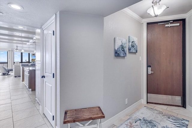 hallway featuring light tile patterned flooring, a textured ceiling, baseboards, and crown molding