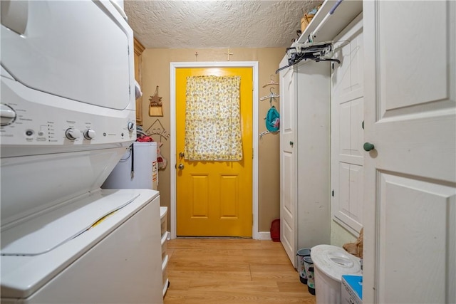 laundry area with stacked washer / dryer, light hardwood / wood-style flooring, and a textured ceiling