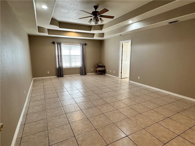 tiled empty room with a textured ceiling, ceiling fan, and a tray ceiling