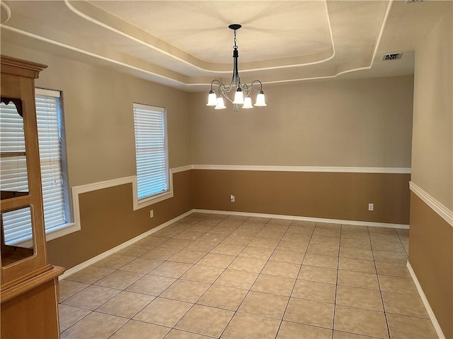 spare room featuring a raised ceiling, light tile patterned floors, and an inviting chandelier