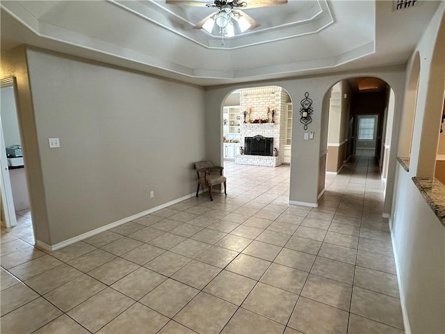 tiled empty room featuring ceiling fan, a fireplace, and a tray ceiling