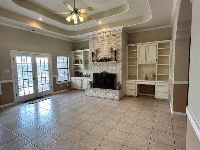 unfurnished living room with a raised ceiling, a brick fireplace, built in desk, and french doors