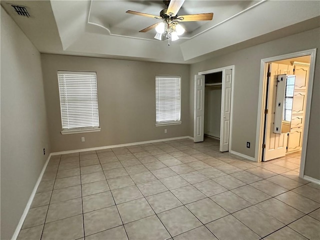 unfurnished bedroom with ceiling fan, a raised ceiling, a closet, and light tile patterned floors