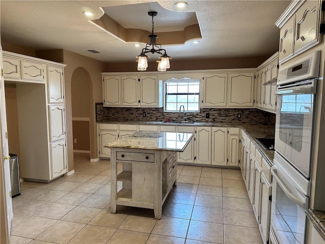 kitchen with a kitchen island, tasteful backsplash, hanging light fixtures, light tile patterned floors, and a raised ceiling