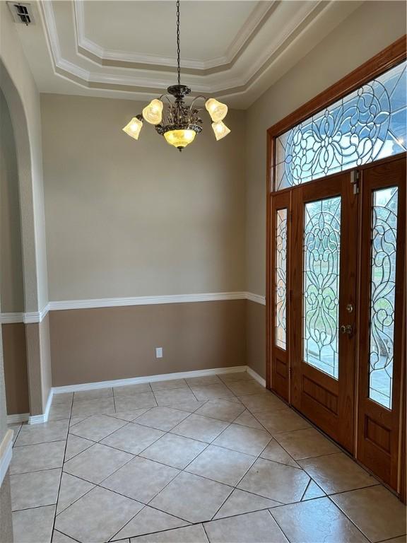 tiled foyer with an inviting chandelier, crown molding, and a raised ceiling