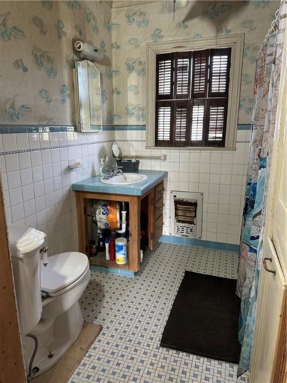 bathroom featuring toilet, heating unit, tile patterned floors, tile walls, and vanity