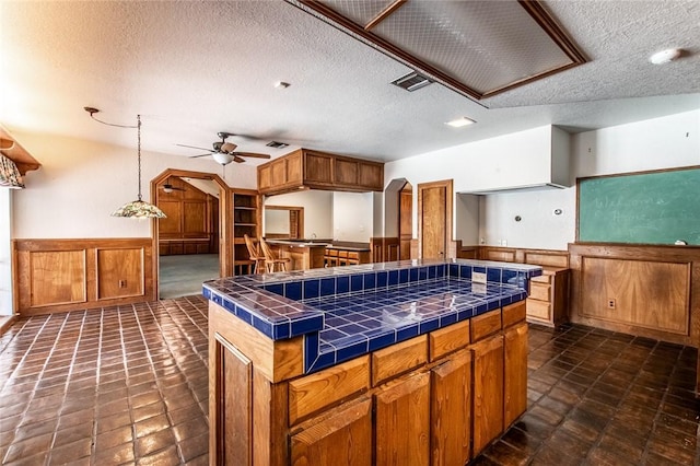 14733 Red River Dr, Corpus Christi, TX 78410 - kitchen with visible vents, ceiling fan, a textured ceiling, wainscoting, and tile countertops