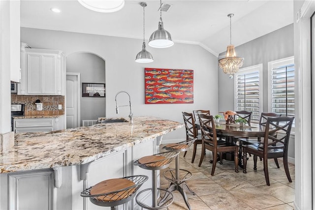 13901 Laffite Dr, Corpus Christi, TX 78418 - kitchen with lofted ceiling, white cabinets, backsplash, light stone countertops, and a breakfast bar