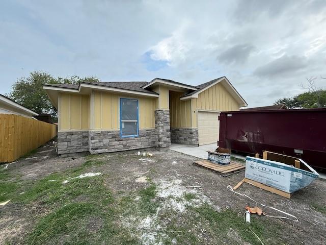 view of front of home featuring board and batten siding, fence, an attached garage, a shingled roof, and stone siding
