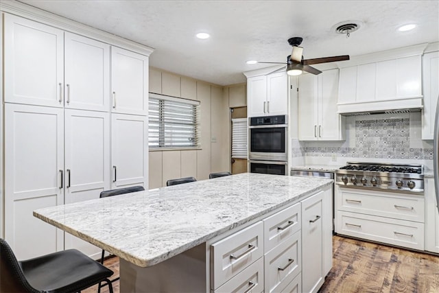 kitchen featuring a breakfast bar area, stainless steel appliances, visible vents, white cabinets, and wood finished floors