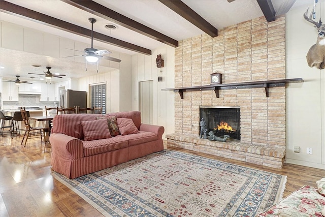 living area featuring visible vents, a ceiling fan, wood finished floors, a fireplace, and beam ceiling