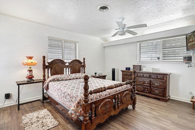 bedroom featuring visible vents, a textured ceiling, multiple windows, and wood finished floors