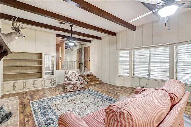 living area featuring a healthy amount of sunlight, ceiling fan, beamed ceiling, and wood finished floors