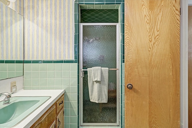 full bathroom with wainscoting, a shower with shower door, tile walls, and vanity