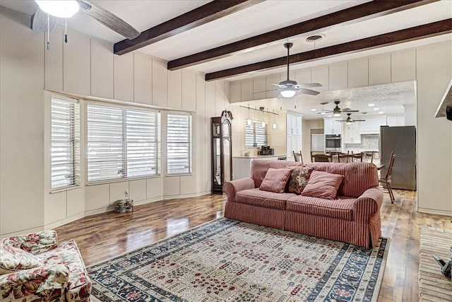 living room with plenty of natural light, visible vents, light wood-style flooring, and beamed ceiling