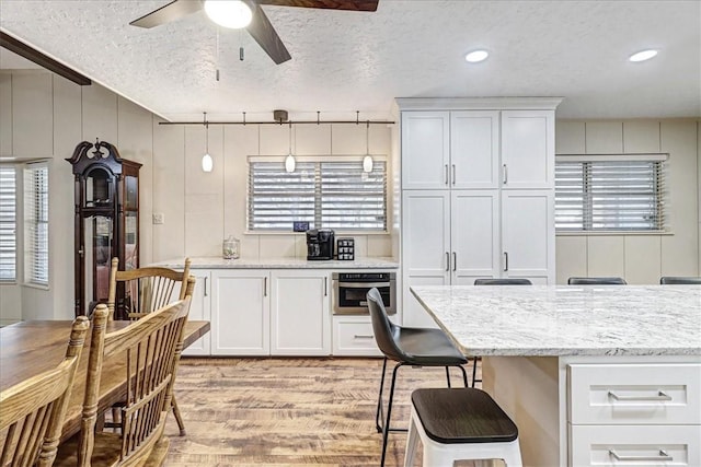 kitchen with a textured ceiling, ceiling fan, oven, white cabinets, and light stone countertops