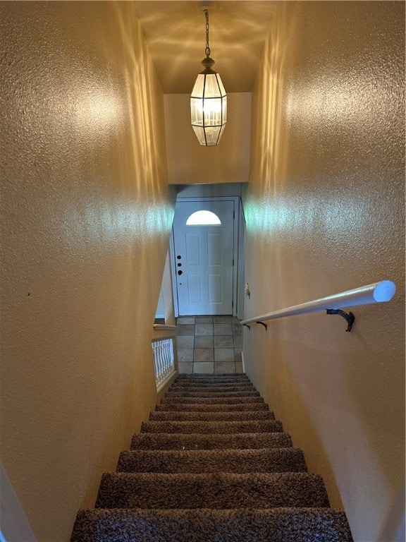 stairway featuring tile patterned flooring and an inviting chandelier