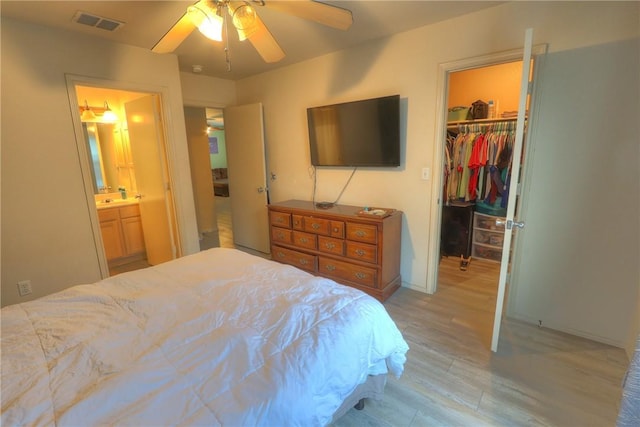 bedroom featuring a closet, visible vents, a walk in closet, ceiling fan, and light wood-type flooring