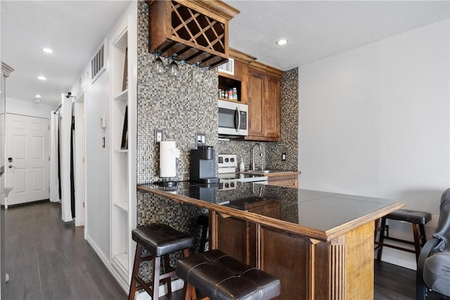 kitchen with tasteful backsplash, dark wood-style floors, a peninsula, stainless steel appliances, and a kitchen bar