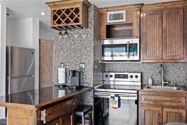 kitchen with visible vents, dark countertops, appliances with stainless steel finishes, a kitchen breakfast bar, and a sink