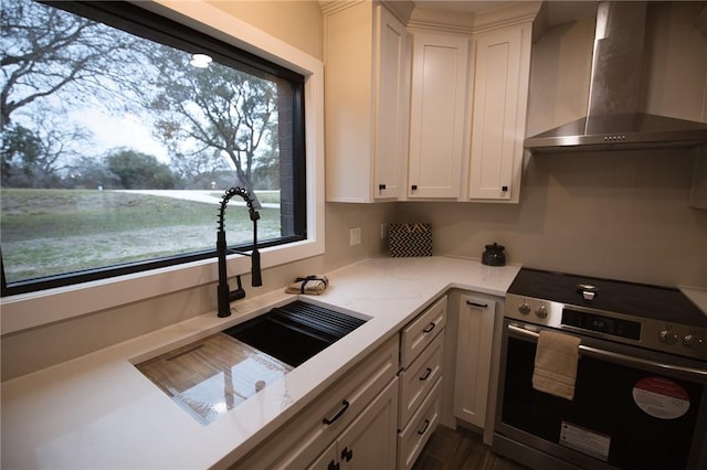 kitchen featuring light stone counters, a sink, white cabinets, wall chimney range hood, and stainless steel electric stove