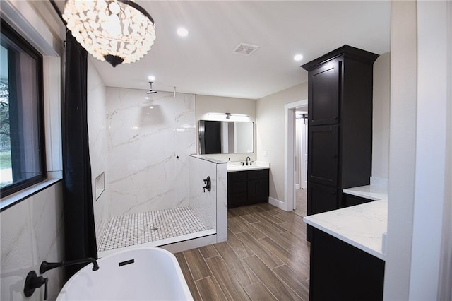 bathroom featuring wood finish floors, vanity, visible vents, a soaking tub, and a marble finish shower