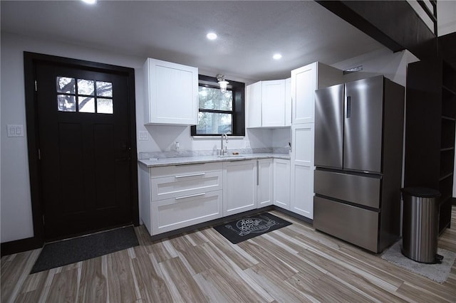 kitchen featuring freestanding refrigerator, light countertops, white cabinetry, a sink, and recessed lighting