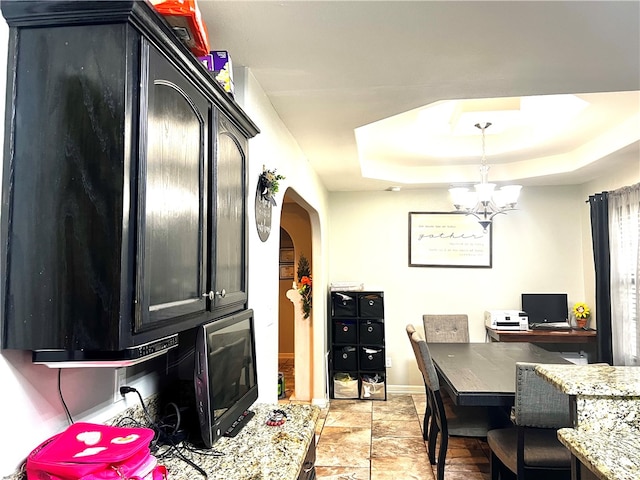 kitchen with hanging light fixtures, a notable chandelier, light stone counters, and a tray ceiling