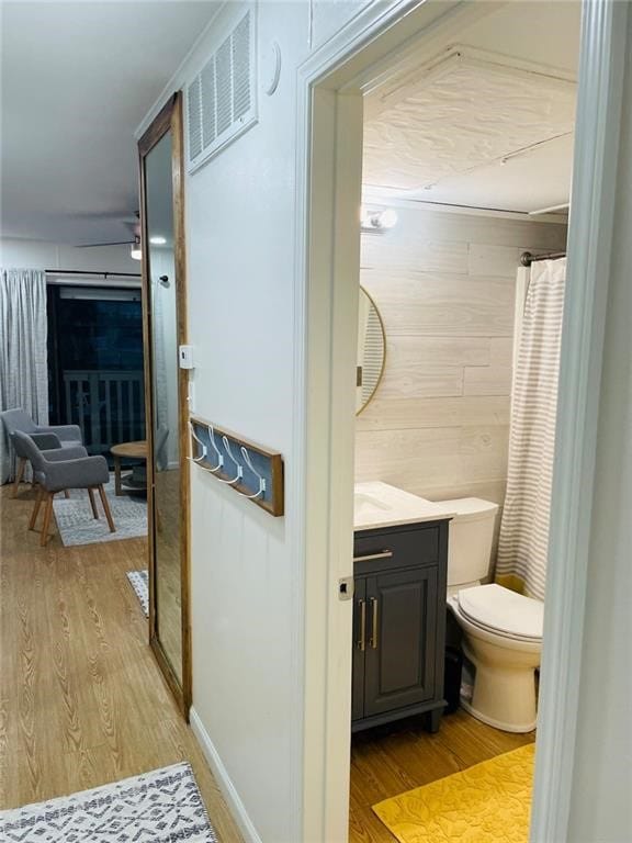 bathroom with hardwood / wood-style flooring, curtained shower, vanity, wooden walls, and toilet