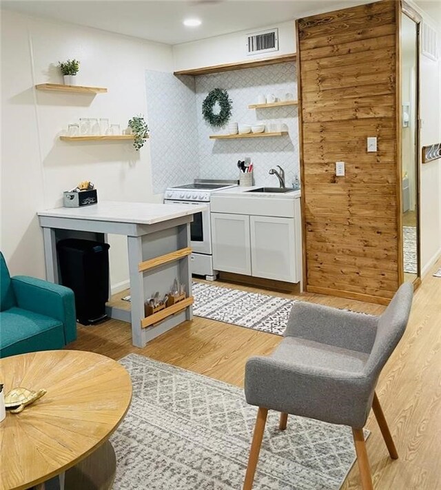 bar featuring sink, backsplash, range, light hardwood / wood-style flooring, and white cabinets