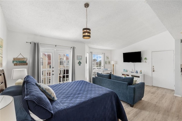 bedroom with vaulted ceiling, light hardwood / wood-style floors, a textured ceiling, access to outside, and french doors