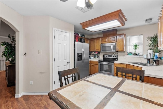 kitchen with arched walkways, a sink, appliances with stainless steel finishes, dark wood-style floors, and brown cabinetry