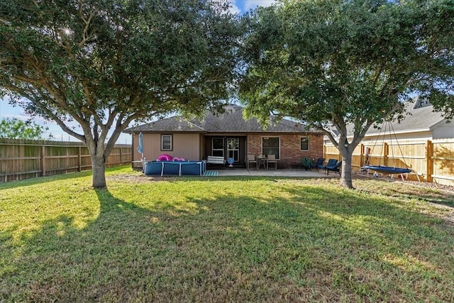 rear view of property with a fenced in pool, brick siding, a yard, a patio, and a fenced backyard