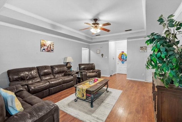 living room with a raised ceiling, visible vents, ornamental molding, ceiling fan, and wood finished floors