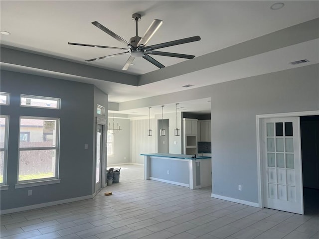 unfurnished living room featuring light wood finished floors, a raised ceiling, visible vents, a ceiling fan, and baseboards