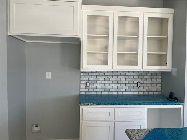 kitchen with glass insert cabinets, dark countertops, white cabinets, and tasteful backsplash