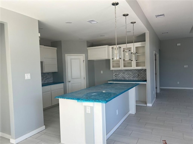 kitchen featuring visible vents, a kitchen island, glass insert cabinets, and white cabinetry