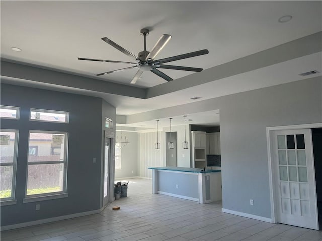 interior space with ceiling fan, visible vents, a raised ceiling, and baseboards