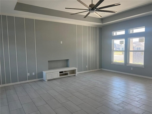 unfurnished living room featuring a tray ceiling, ceiling fan, and baseboards