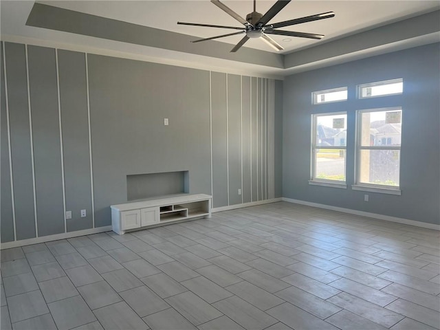 unfurnished living room with a tray ceiling, baseboards, and a ceiling fan