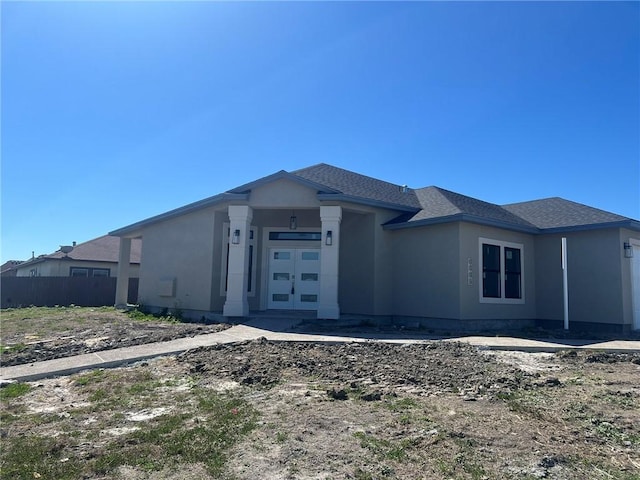 view of front of house with roof with shingles, fence, and stucco siding