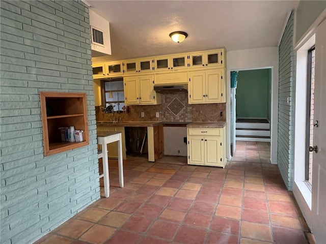 kitchen featuring tasteful backsplash, cream cabinets, and brick wall