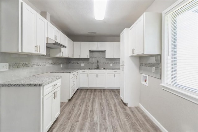 1337 Daytona Dr, Corpus Christi, TX 78415 - kitchen featuring under cabinet range hood, a sink, light wood-style flooring, tasteful backsplash, and white cabinetry