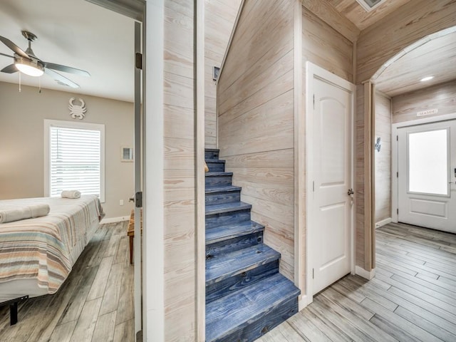 stairway with ceiling fan, wood walls, and hardwood / wood-style floors